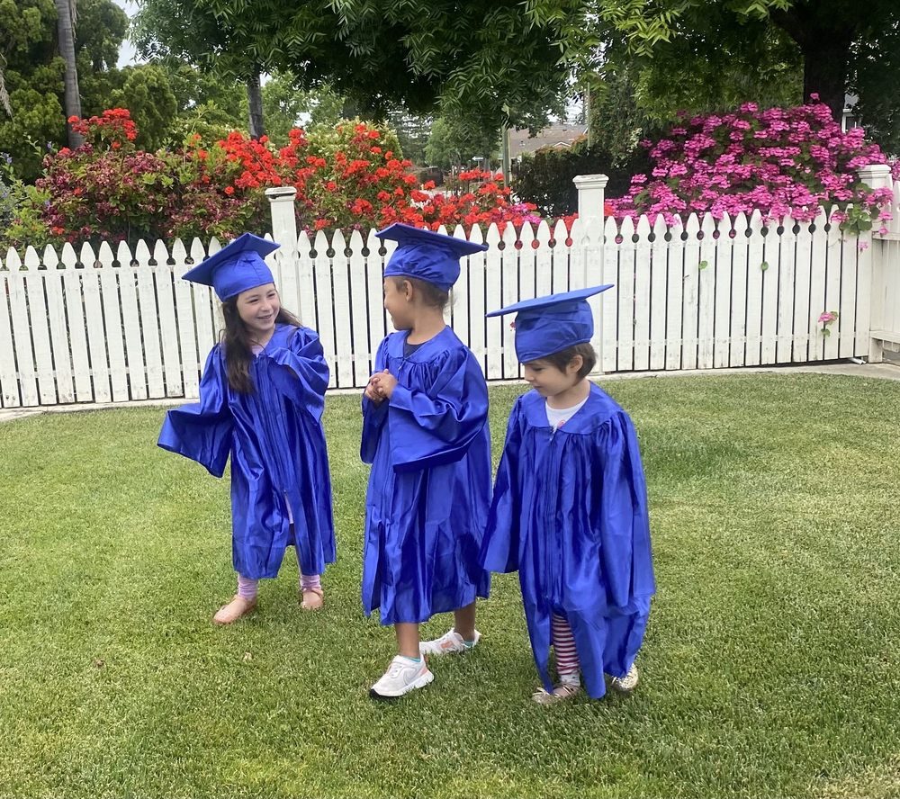 Three preschoolers in blue caps and gowns on graduation day in the backyard